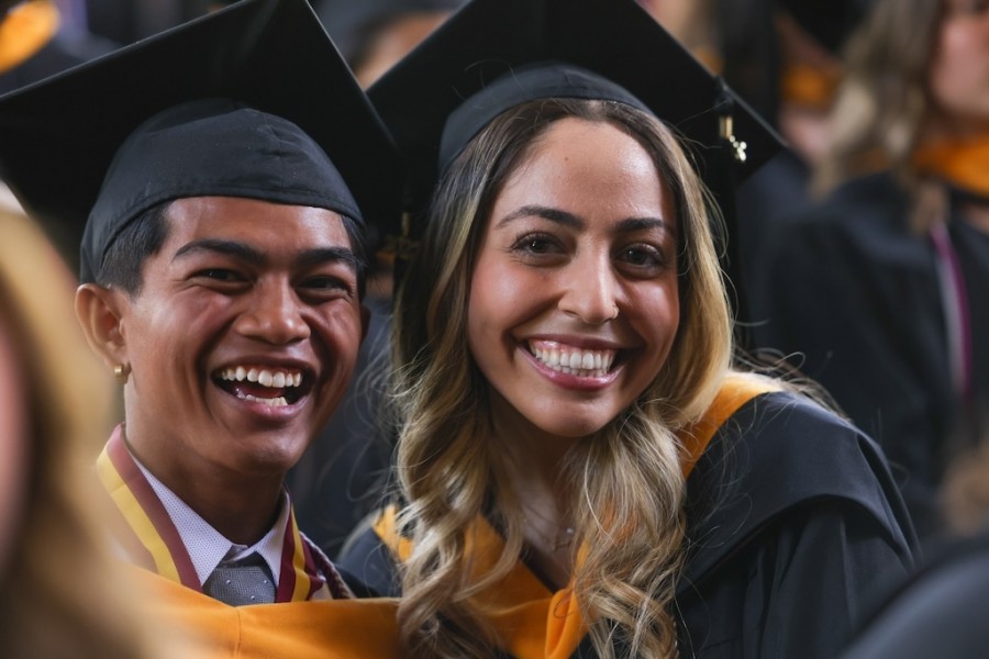Two students smile in cap and gown at graduation