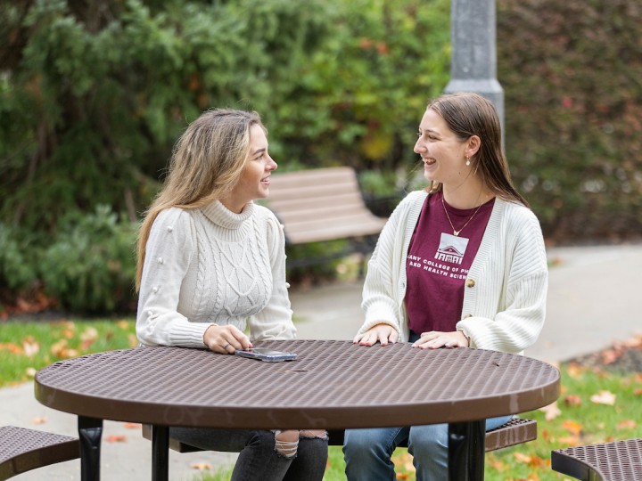 Two students sit outside at a table during a beautiful fall day