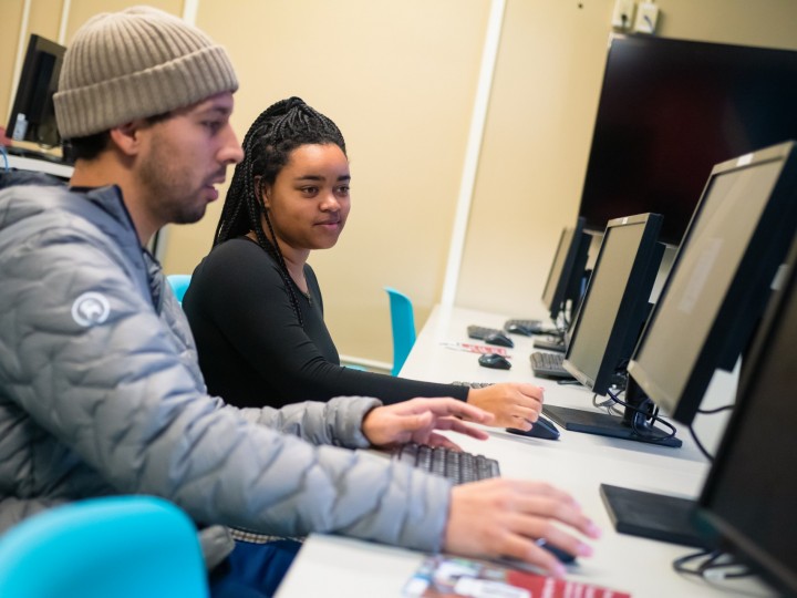 Two students sit together at computer during class