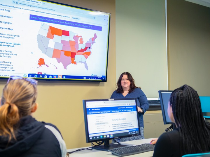 A faculty member presents to a group of students displaying a public health map on screen