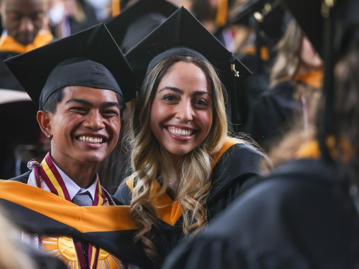 Two students wearing caps and gowns pose for photo at Commencement