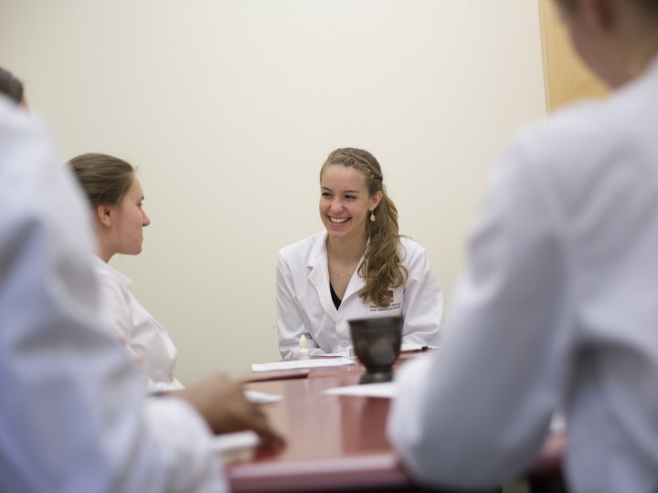 Students sitting around the table in white coats during lab coursework