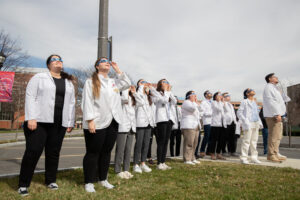Students stand outside in white coats with glasses for the Solar Eclipse