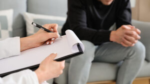 A doctor sits with clipboard and pen and talks to patient