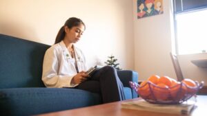 A student sits on coach with laptop next to a table with oranges