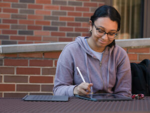 A student sits outside on campus with tablet