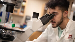 A student looks into a microscope in a lab coat
