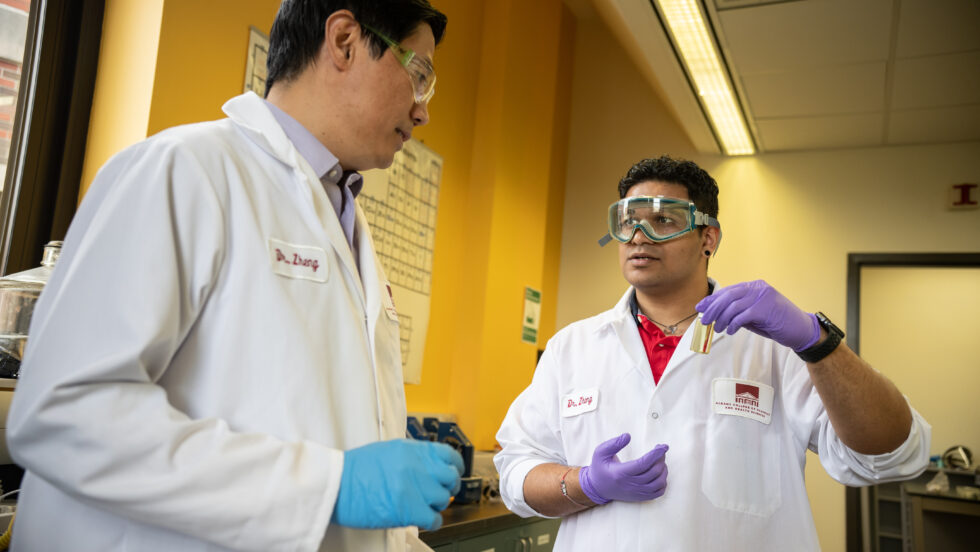 Dr. Zheng and student wear lab safety gear while having a conversation