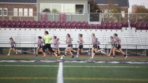 Female players running down the field with the bleachers in the background