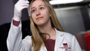 Student dressed in white holds sringe in hand towards the sky