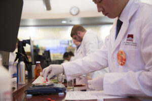 Student in white coat and gloves weighing red capsules on the benchtop scale