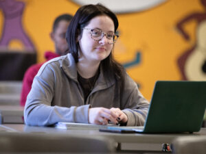 Student smiles in classroom with laptop on table