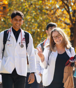 Students in white coats smile and wave as they walk to class