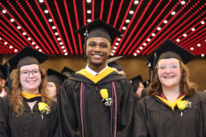 Students smile in cap and gown at commencement ceremony