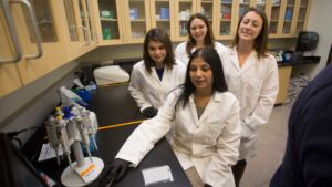 Students stand behind Dr. Malik in white coats