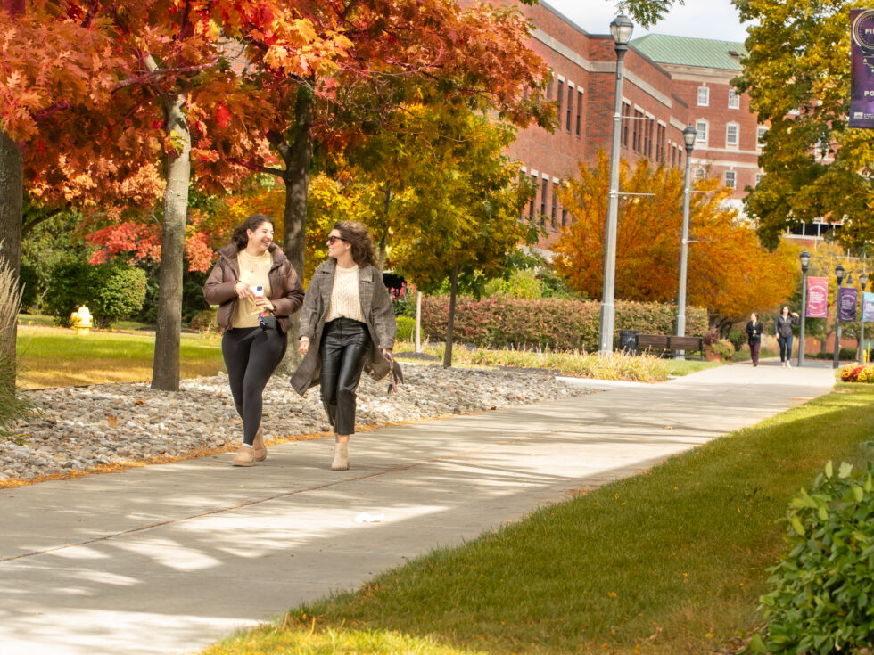 Two students walk across campus on a beautiful Fall day