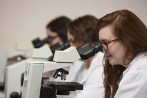 Three women in shite coats using microscopes to examine slides