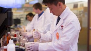 A student wears white coat and gloves with mortar and pestle