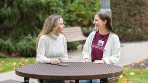 Two students sit on an outside bench and laugh together