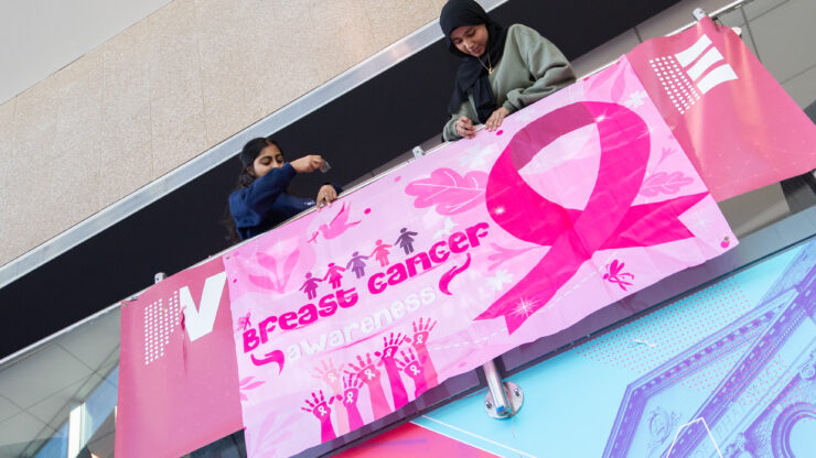 Two female students hang a breast cancer awareness banner in the atrium.