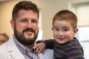 An MS in CLS student celebrates with his toddler son after receiving his white coat