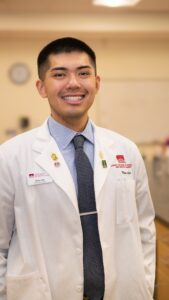 Photo of PharmD candidate, Nico Lee, Class of 2026, wearing a white coat in a lab